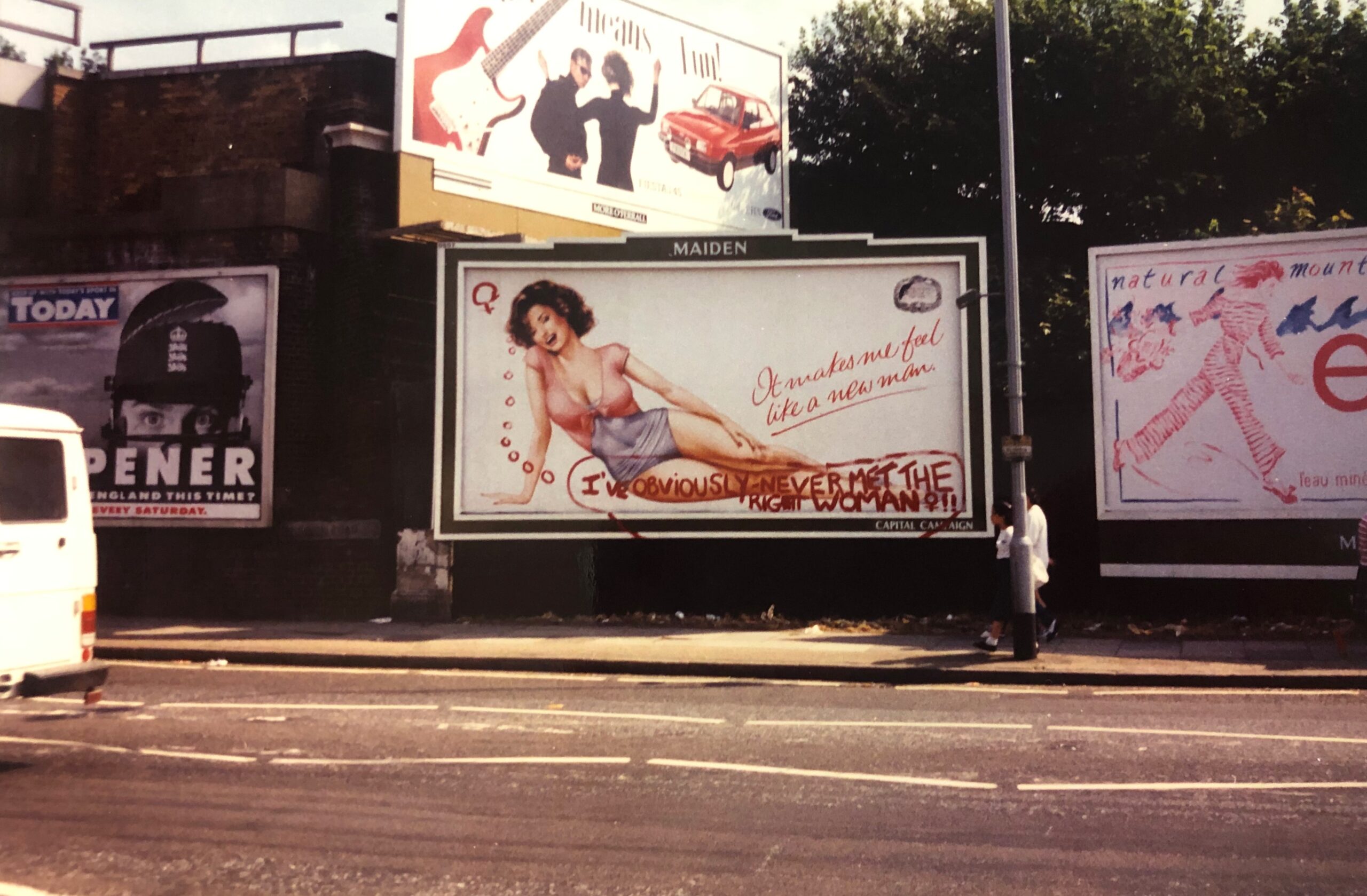 Billboard advert featuring a pin-up-style woman and the caption, 'It makes me feel like a new man!'. Below this, in red paint, a thought bubble: 'I've obviously never met the right woman!!' 