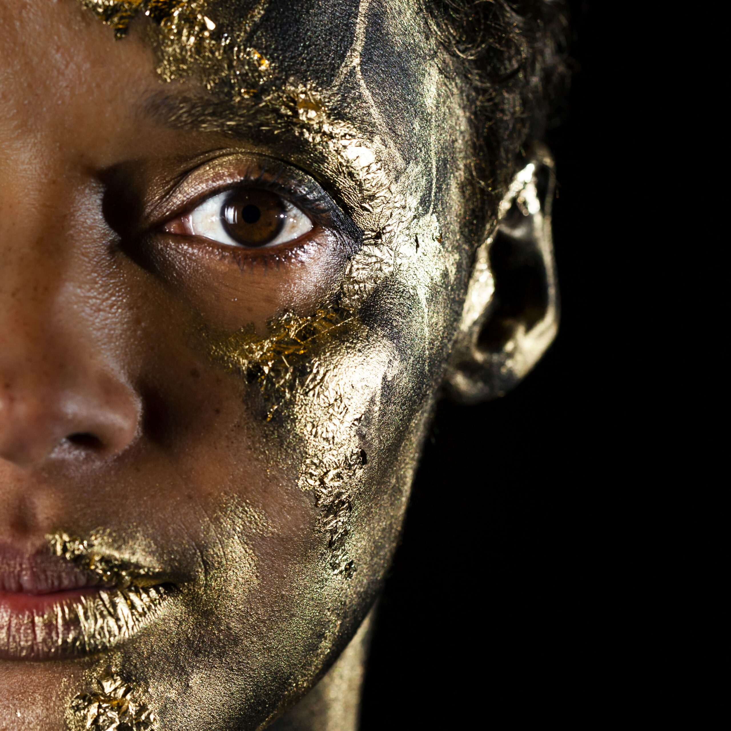 Close up image of half of a person's face which is painted in gold