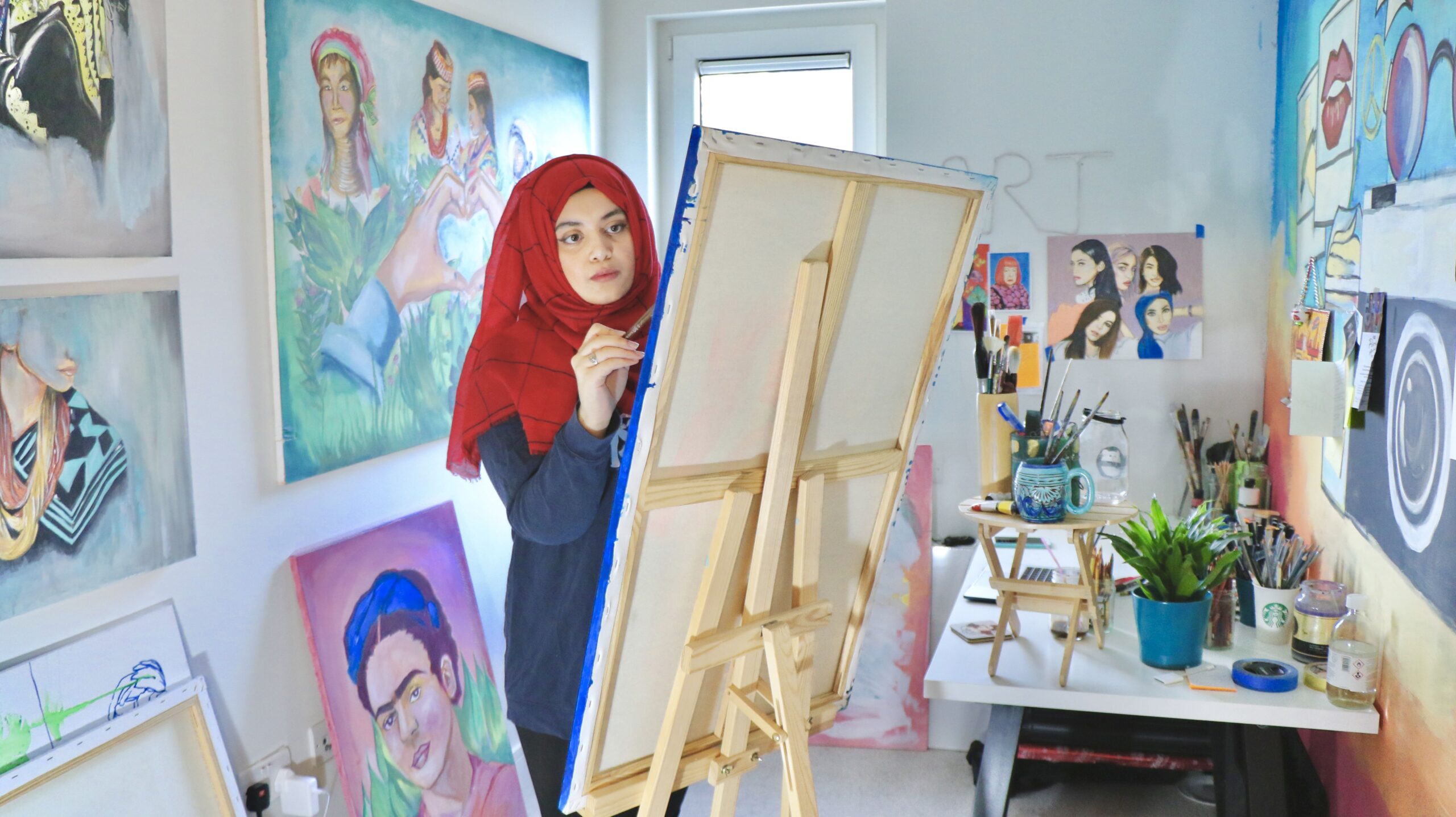 Maliha Abidi painting on a canvas in a studio full of paintings of women