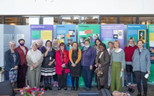 Colour image of a group of women standing in a line in front of museum exhibition panels. 