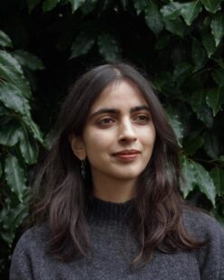 Portrait of Roshni Gallagher, taken from the shoulders up, against a backdrop of dark foliage.