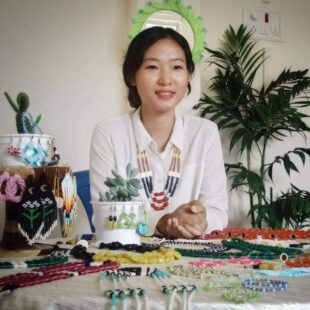 Artist Sumiho, Naga Jewellery artists sits surrounded by bead necklaces and other items. 