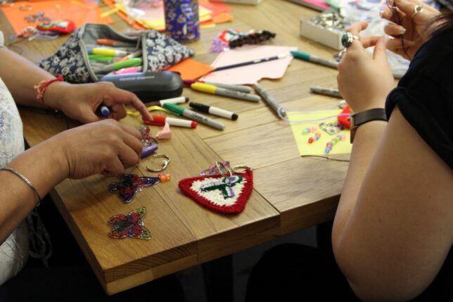 Table with pens, paper, knittting, and hands making things