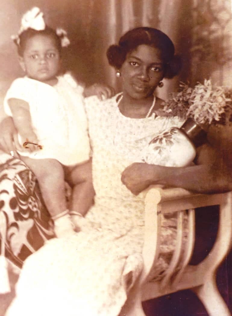 An old sepia photograph of a woman holding a child and sitting with a vase of flowers in the other hand