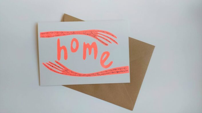 Two neon orange arms extend from either side of the card. The word Home is written in the same colour and looks cradled between the arms.