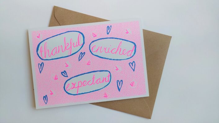 The words Thankful, Enriched and Expectant are writing in bright pink, and circled in blue. Around the words there are small blue hearts on a bright pink background.