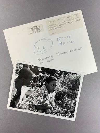 two photographs on a grey background, one showing the back and writing on the back, one showing a man and a woman in nature looking at one another. 