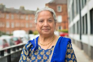 A photograph of Trishna Singh OBE. She faces the camera and is wearing a blue and gold sari