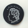 Circular logo patch with the Women in Profile logo of a women's head in profile with a halo of sparks, in white on black