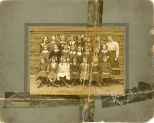 An old sepia photograph of students at Golfhill Public School. It is a formal school photograph with children in uniforms sitting in rows with their school mistress standing to the right of them