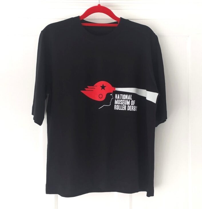 Black t-shirt featuring the NMRD logo, featuring a woman's head wearing a red winged helmet with a beam of light coming from the front, and the words 'National Museum of Roller Derby'