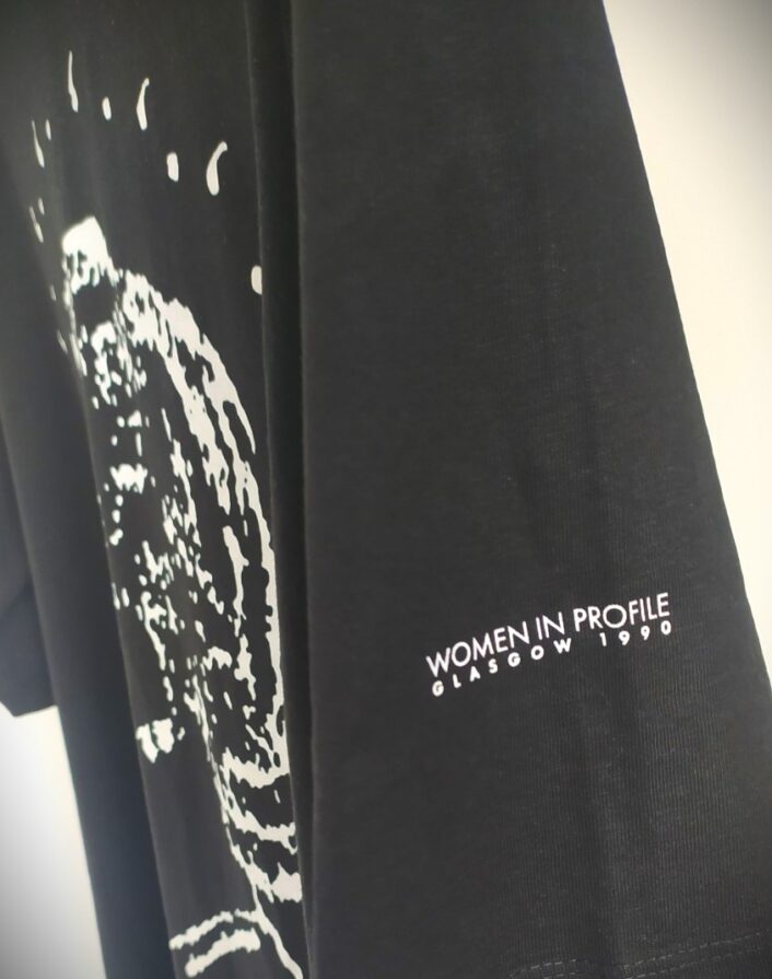 Detail of the Women in Profile logo t-shirt sleeve, with the words 'Women in Profile / Glasgow 1990'