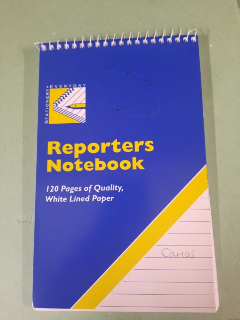 Photo of a reporters notebook of the kind which can be brought in newsagents or supermarkets. It's blue and yellow, with the word "Camas" on the front.