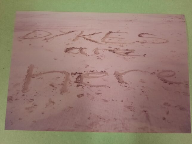 Photo of the words "dykes are here" written on a sandy beach