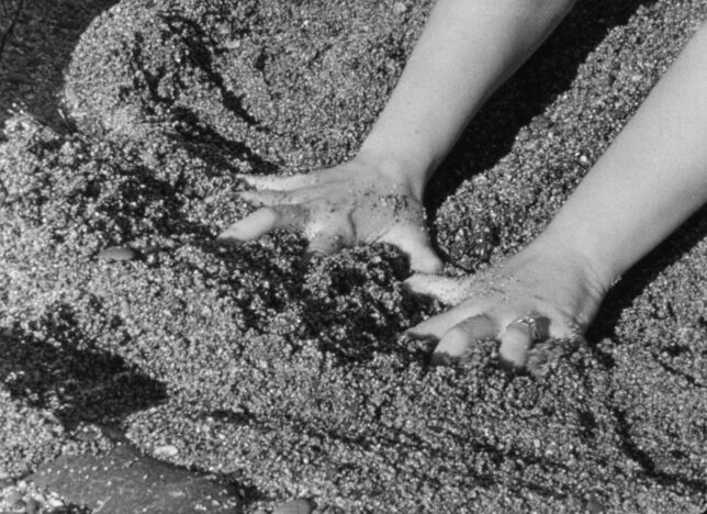 Black and white photograph of two hands pushing into sand