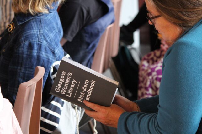 A photo of a person reading a physical copy of the Handbook to Net Zero.