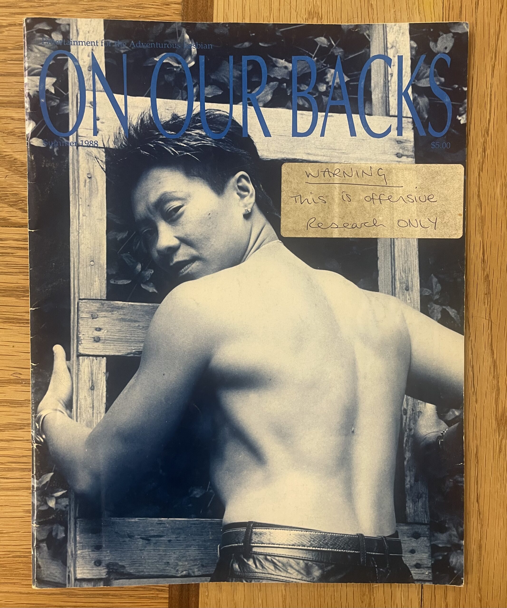 Cover of On Our Backs magazine from the GWL archive. The cover is an image of a topless butch person looking over their shoulder. There is a label stuck to the magazine cover that reads: Warning This is offensive, Research ONLY