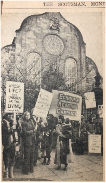 black and white photograph showing a group of around 10 individuals holding signs reading ‘whose life? The unborn or the living’ and ‘Edinburgh Abortion Campaign’.