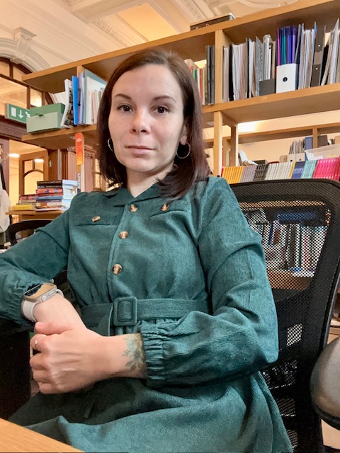 Yuliia Babenko sitting in a chair in the office wearing a green dress with buttons and a belt