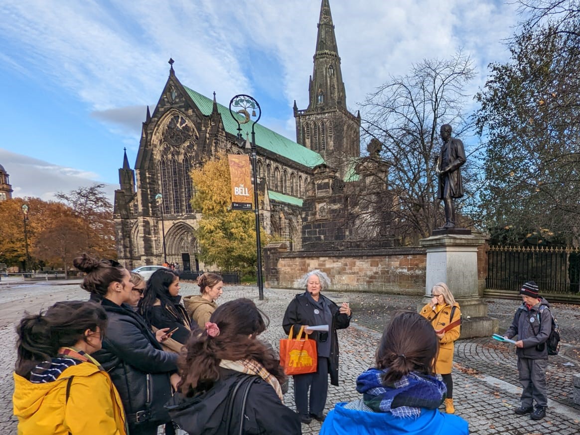 A tour guide speakers to walk attendees in front of Glasgow Cathedral.