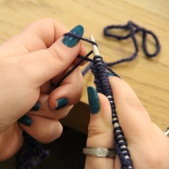 Two hands holding knitting needles, demonstrating a cast on.