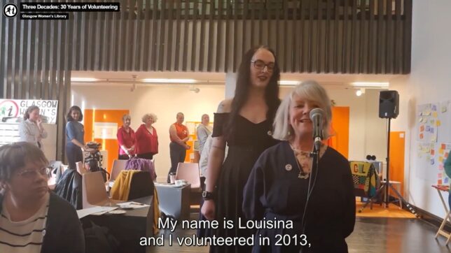 Screenshot from the Three Decades of Volunteering video: a volunteer called Louisina introduces herself into a microphone.