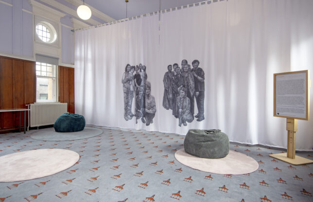 Photo of community room with a large curtain with illustrations printed on it. The community room is filled with soft furnishings and lavender colours.