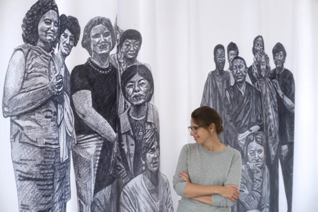 Photo of Illustrations on curtain with Olivia Plender standing in front.