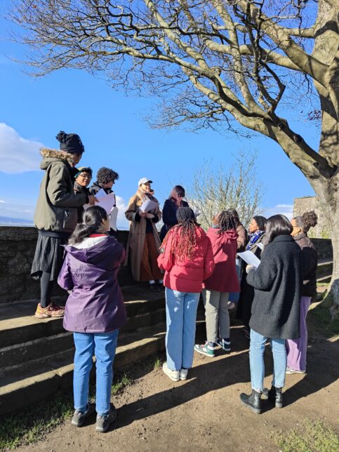 The readers gathered together on a raised stone surface at the Queen Anne Gardens, with a view overlooking the city.