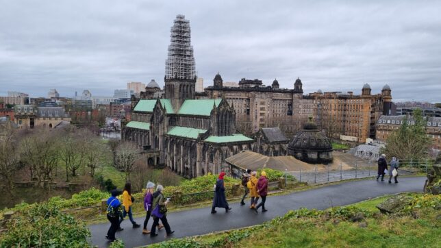 Photograph of a 10 people walking along a path in the Necropolis with Glasgow Cathedral in the background