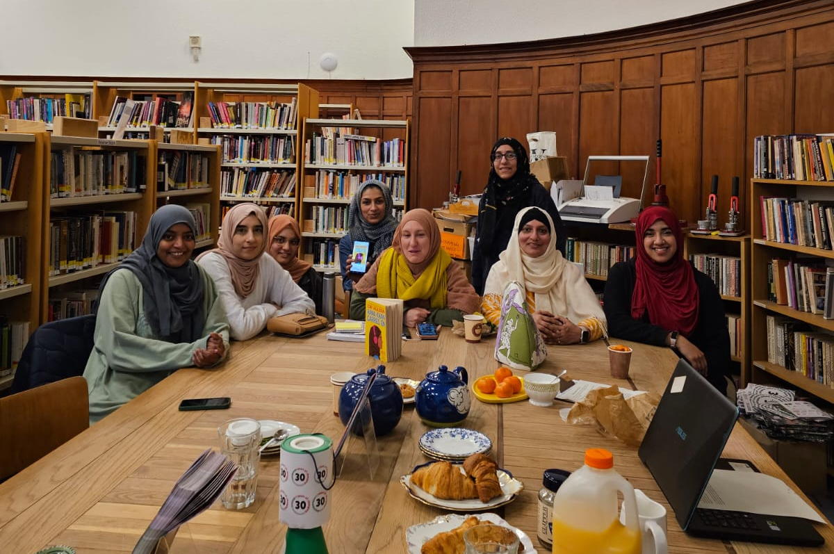 7 Muslim women sit around The Hub in Glasgow Women's Library, surrounded by books, snacks and tea