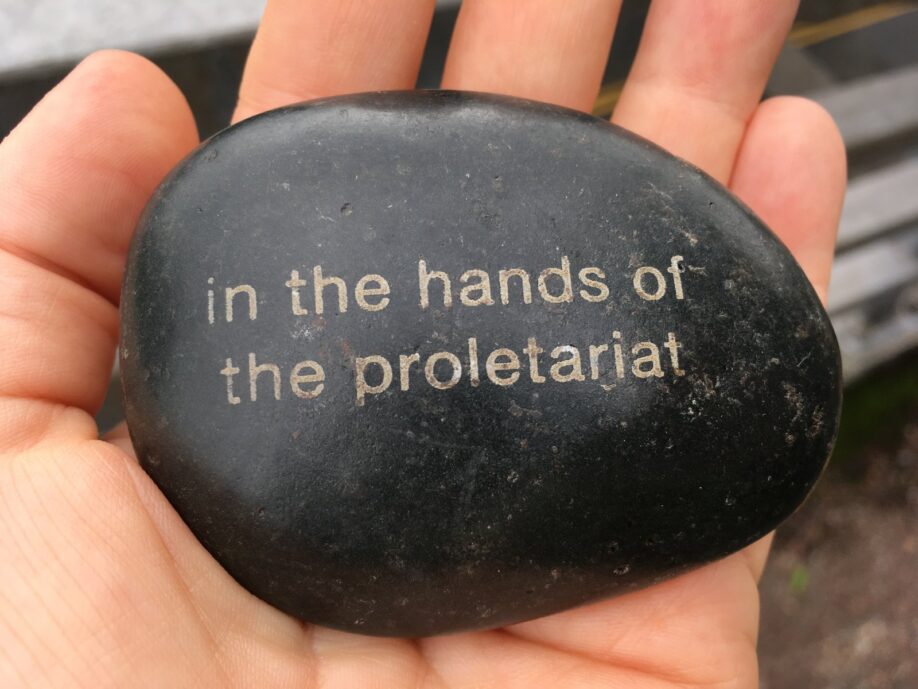 A black stone being held in someone's hand, carved with the words "in the hands of the proletariat"