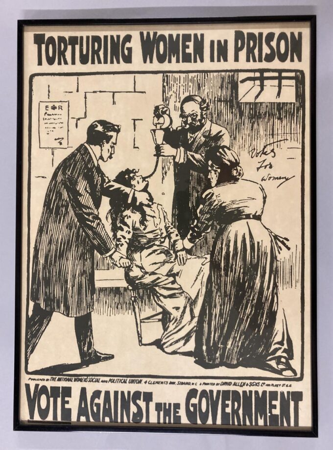 Black and white poster titled "Torturing Women in Prison". Below the title is an image of two men and a woman holding another woman down whilst forcibly feeding her via a tube down her nose. At the bottom are the words, "Vote Against the Government"