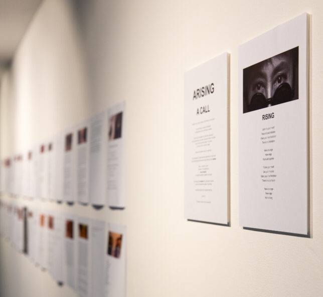 view on a white gallery wall at GWL showing two lines of A4 papers attached to the wall, each sheet has an image at the top. Next to these we see instructions in poem form by Yoko Ono and an image of her eyes with sunglasses.