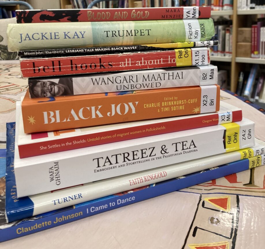 A pile of books written by Black writers stacked on a table in the library. The titles include Trumpet by Jackie Kay, All About Love by bell hooks, and Unbower by Wangari Maathai