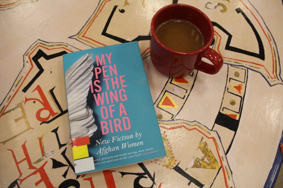 Image of the anthology "My Pen is the Wing of a Bird" placed on table, next to it is cup of coffee