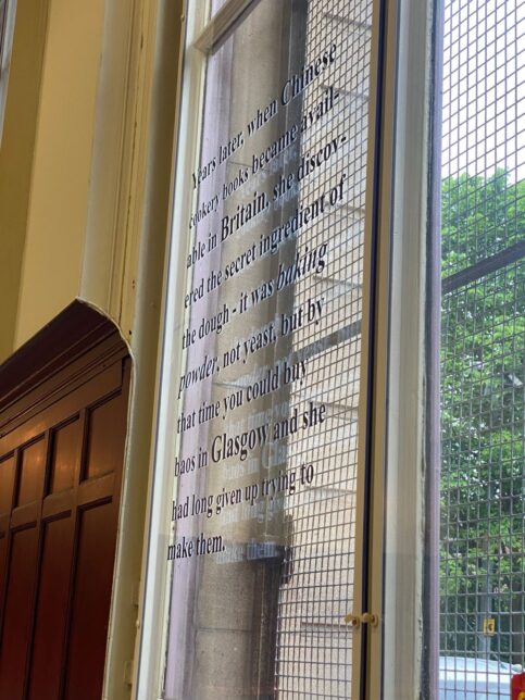 Vinyl text on window in with light shining through, reads: 'Years Later, when Chinese cookery books became available in Britain, She discovered the secret ingredient of the dough- it was baking powder, not yeast, but by that time you could buy baos in Glasgow and she had long given up trying to make them.'