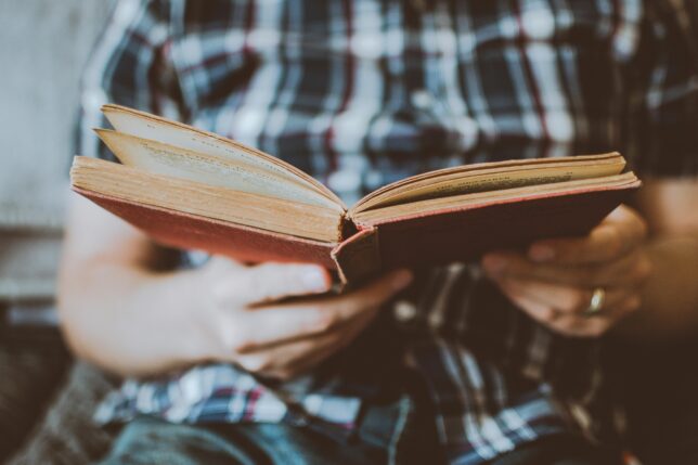 Hands hold an open book being read.