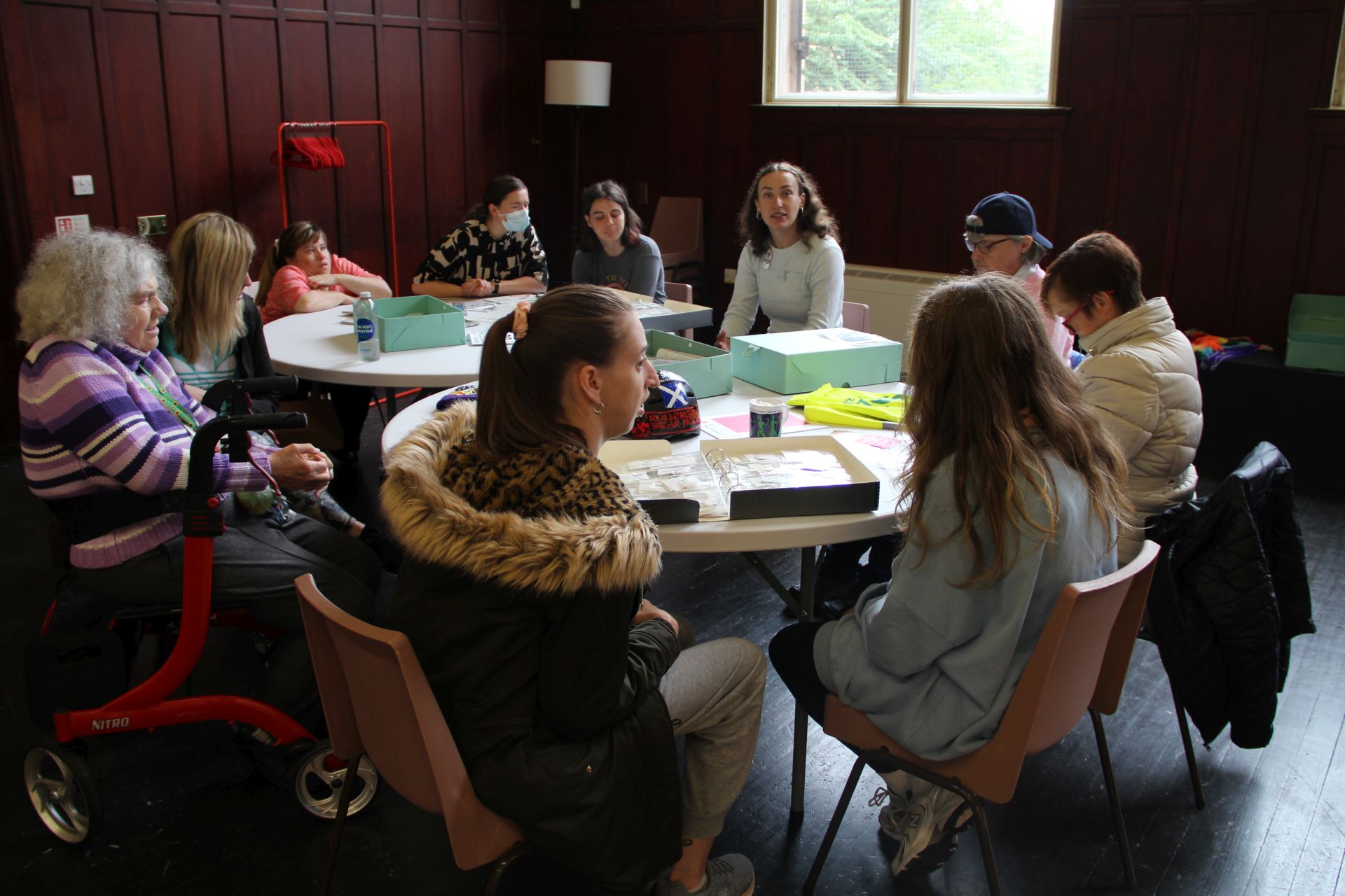 Visitors sit at round tables covered in archive boxes, looking at archive material.