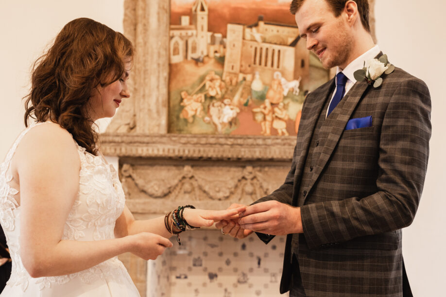 Photo of a groom placing a wedding ring on the bride's ring finger.