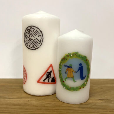 A large candle with several logos from GWL's past, next to a small candle with a festive-themed version of the GWL logo.