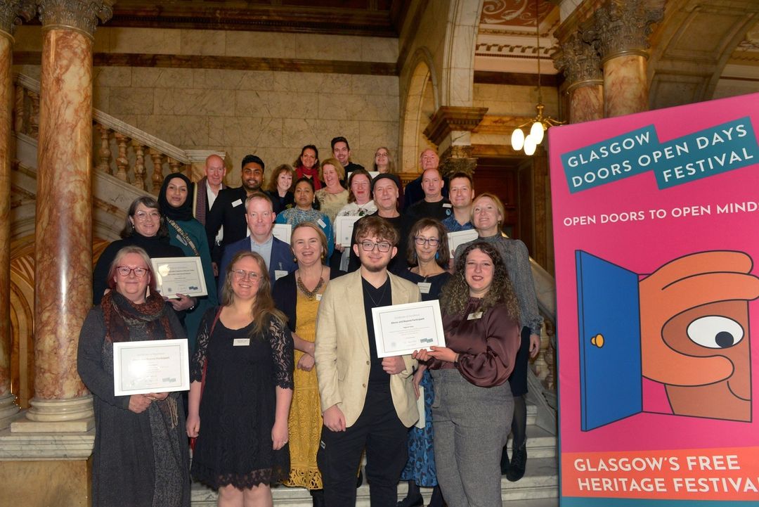 many people standing on the marble steps inside the Glasgow City Chambers, many of whom are holding on to framed awards