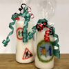 A large candle with several logos from GWL's past, next to a small candle with a festive-themed version of the GWL logo. Both are wrapped in cellophane and tied with ribbons.