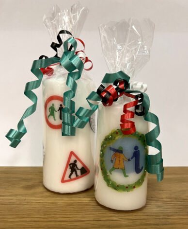 A large candle with several logos from GWL's past, next to a small candle with a festive-themed version of the GWL logo. Both are wrapped in cellophane and tied with ribbons.