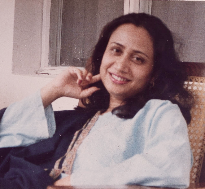 Urdu poet Perveen Shakir smiles at the camera, she is wearing a light coloured tunic, and has dark brown hair.