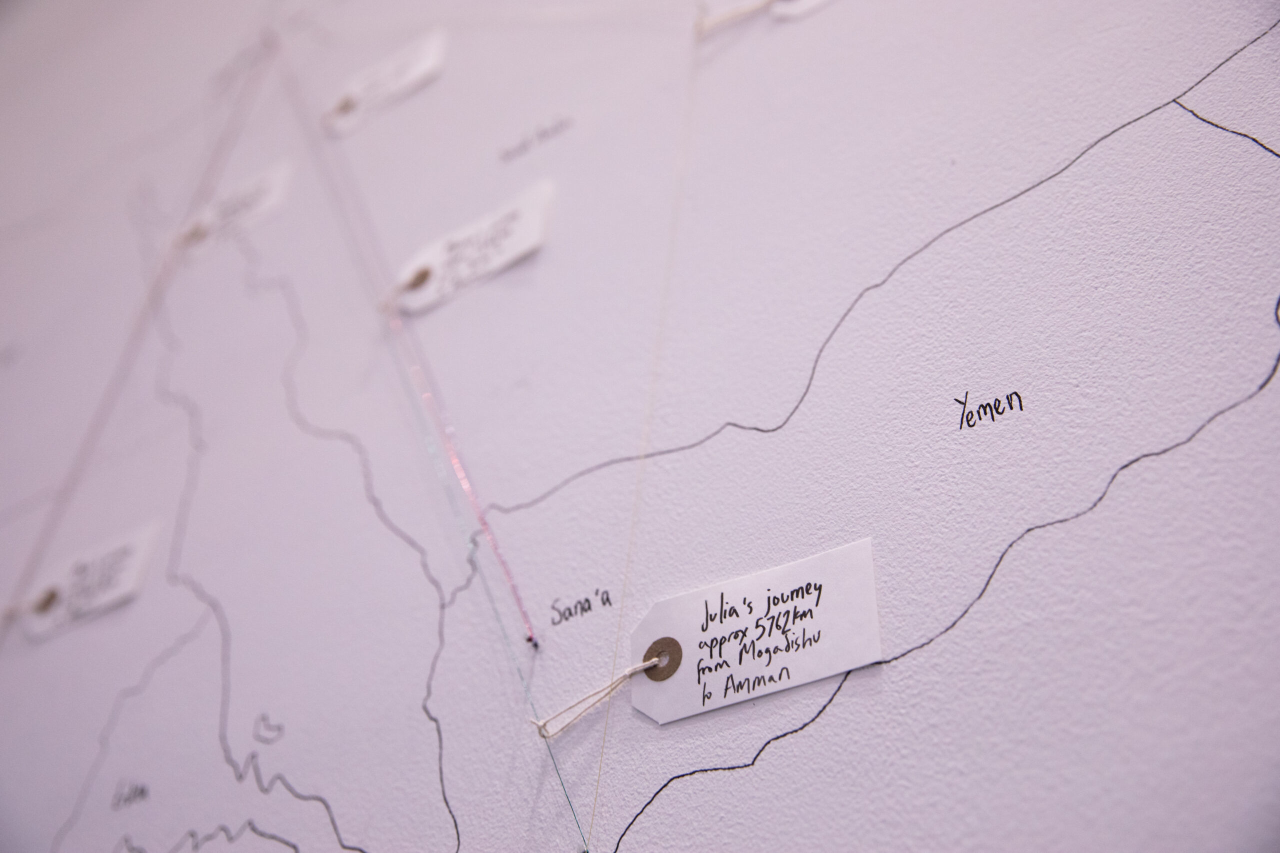 A white wall with a map drawn in black pen of Jordan and the countries surrounding it. This is a close up of the map showing Yemen and a paper tag reading 'Julia's journey approx 5762 km from Mogadishu to Amman, Jordan