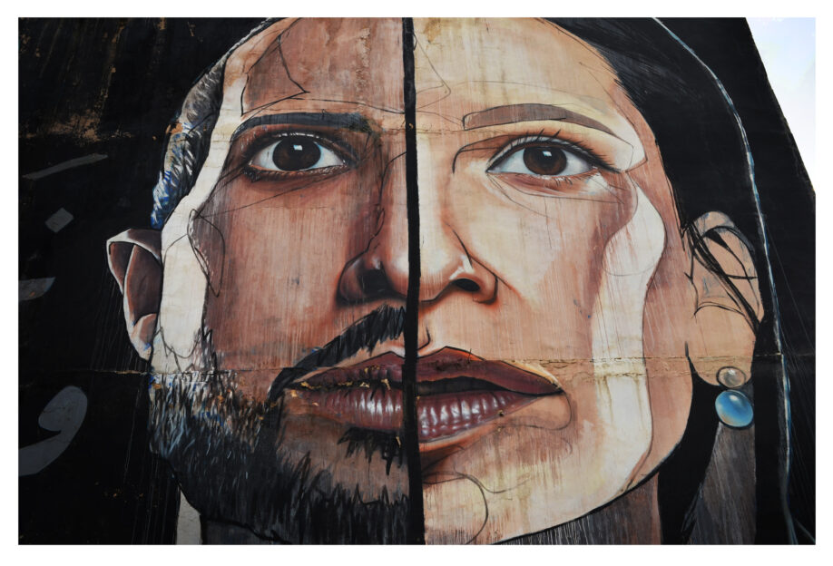 A mural on a wall in Amman, Jordan, depicting half of a face of a male-presenting person alongside half of the face of a female-presenting person.