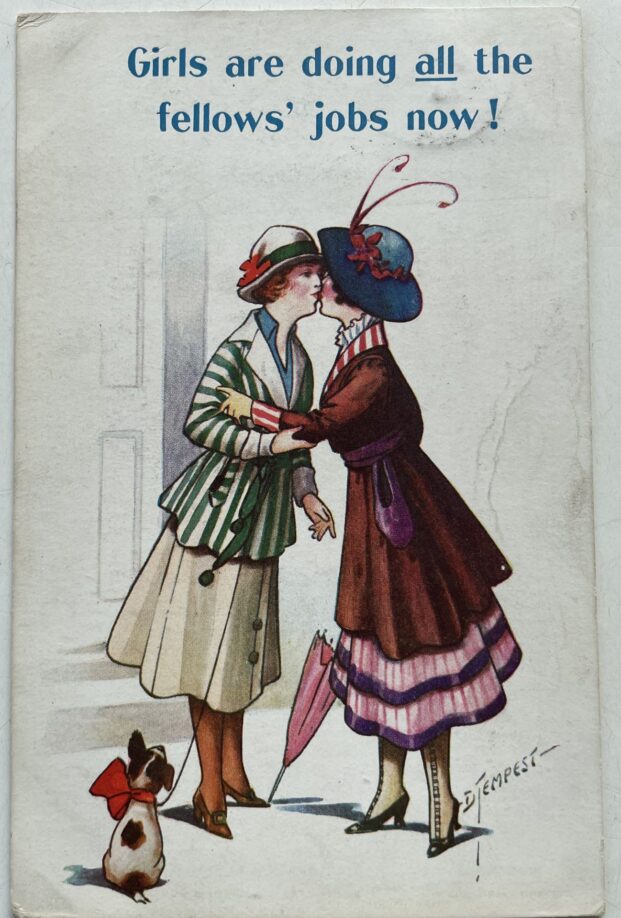 An illustrated postcard of two young women sharing a kiss as a small dog with a bow looks on. The women appear fashionably dressed in 1910s mid-calf length dresses and decorated hats. The postcard is captioned "Girls are doing all the fellows' jobs now!" (the 'all; is underlined).