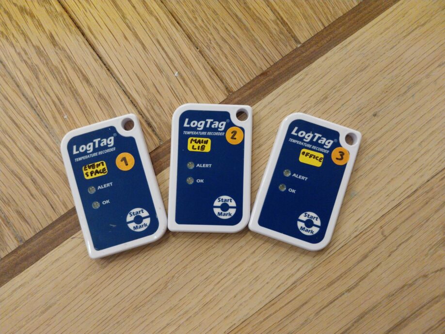 Three blue and white LogTag recorders on a wooden table - labelled as "Event Space", "Main Lib" and "Office"