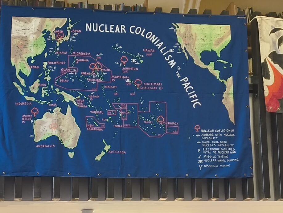 A wall hanging hung from the mezzanine rail, showing a map of the Pacific with nuclear testing sites marked.